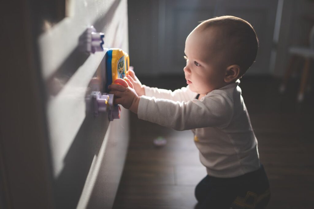 pexels photo 9328014 A cute baby exploring magnetic toys on a cupboard, illuminated by natural light indoors.